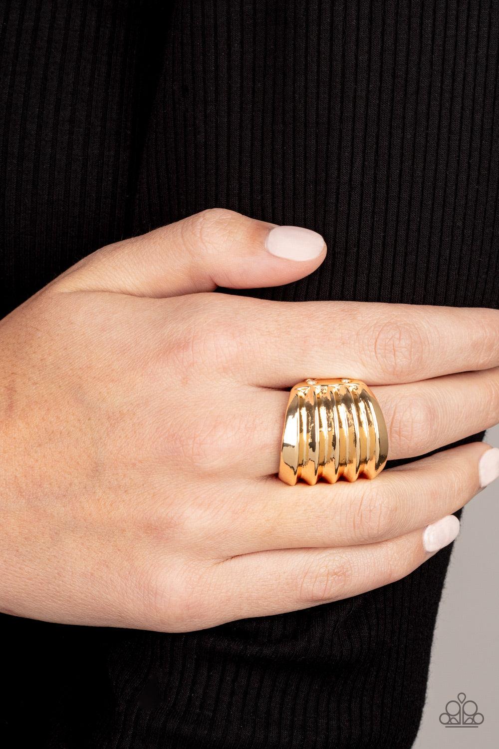 Paparazzi Accessories Hit Em Where It Hurts - Gold Rippling gold bands coalesce into a thick frame around the finger for a dramatic industrial look. Features a stretchy band for a flexible fit. Sold as one individual ring. Jewelry