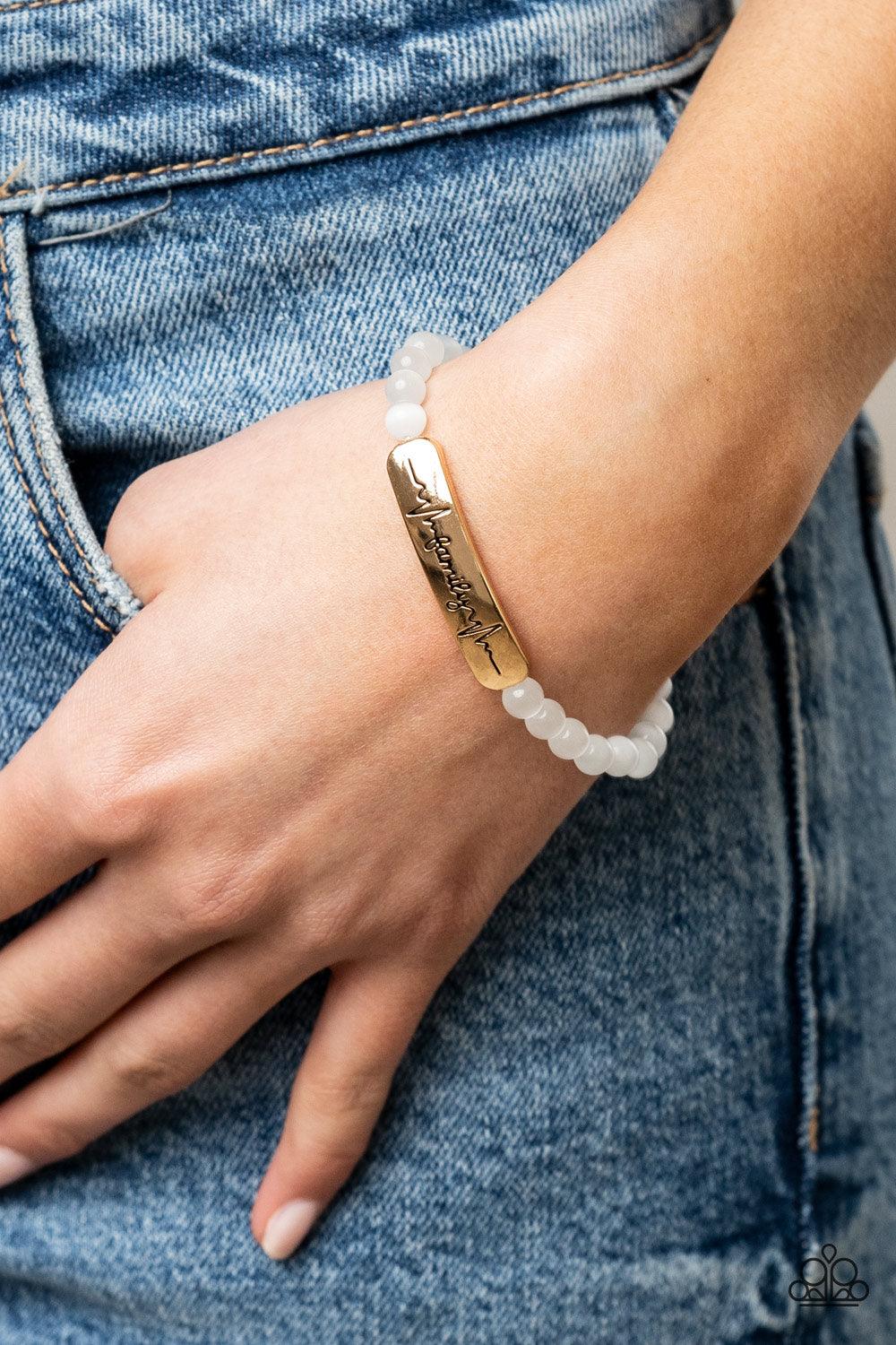 Paparazzi Accessories Family is Forever - Gold Stamped in heartbeats and the word, "Family," a glistening gold plate attaches to a strand of white cat's eye stone beads that are threaded along a stretchy band, creating a whimsically sentimental centerpiec