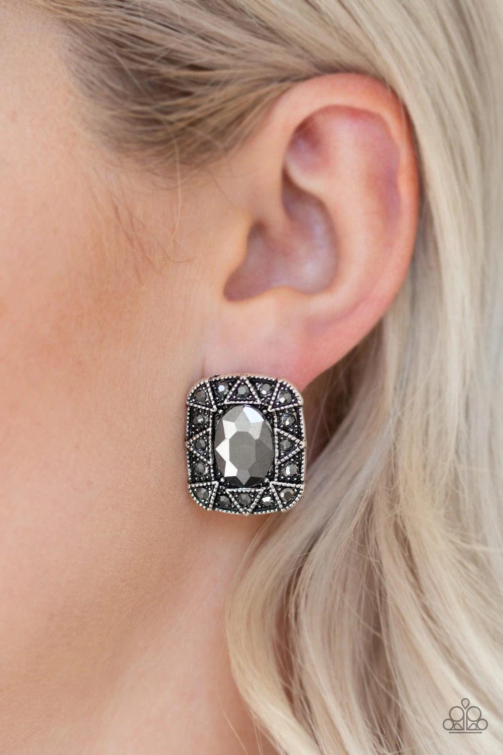 Paparazzi Accessories Young Money - Silver An oval hematite gem is pressed into a square silver frame radiating with glittery hematite rhinestones and triangular patterns for an edgy refinement. Earring attaches to a standard post fitting. Sold as one pai