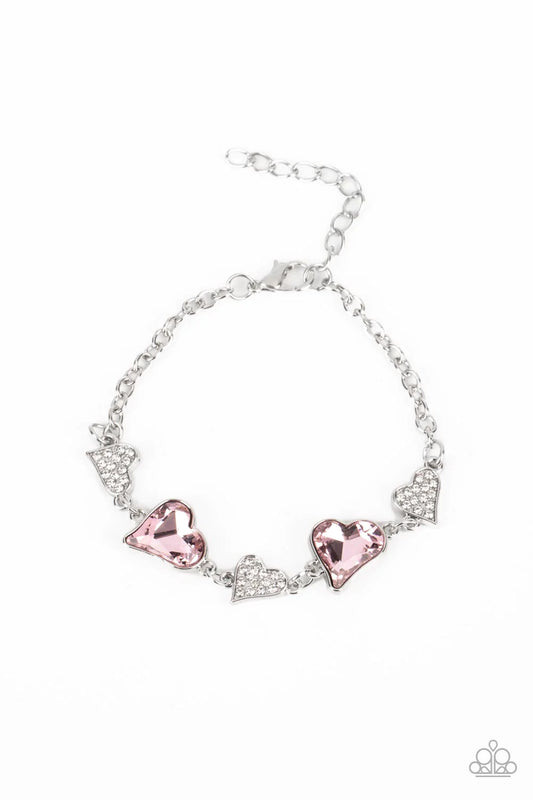 Paparazzi Accessories Cluelessly Crushing - Pink An asymmetrical collection of hearts coalesce around the wrist in this flirty centerpiece. Three of the silver hearts are encrusted with dainty white rhinestones, while the other two heart frames boast soft