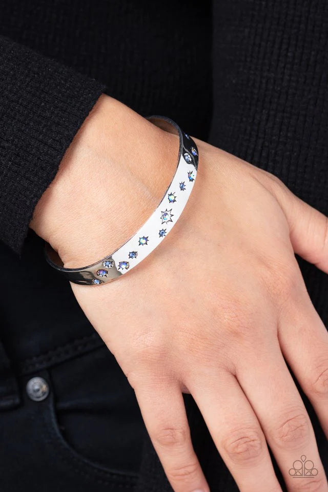 Paparazzi Accessories Starburst Shimmer - Blue Tinted in subtle, stellar shades of blue and iridescence, dainty rhinestones are pressed into the centers of stamped stars in varying sizes. Embossed in tactile textures, the starry collection wraps around th
