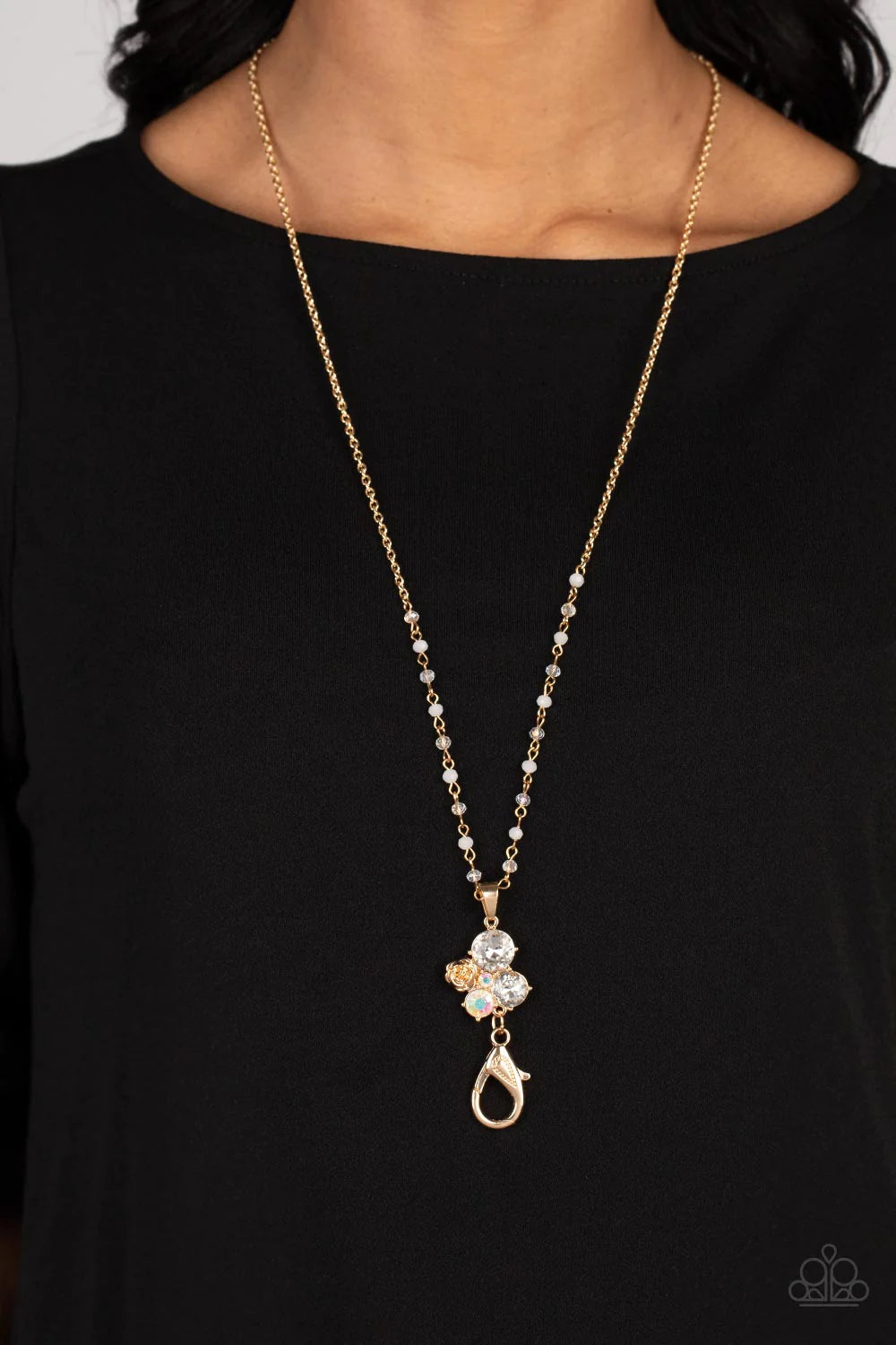 Paparazzi Accessories Rainbow Bloom - Gold *Lanyard Varying in size and shimmer, rhinestones brushed in an iridescent shimmer and glittery white rhinestones coalesce into a clustered pendant at the bottom of a shimmery gold chain. A metallic gold rose blo