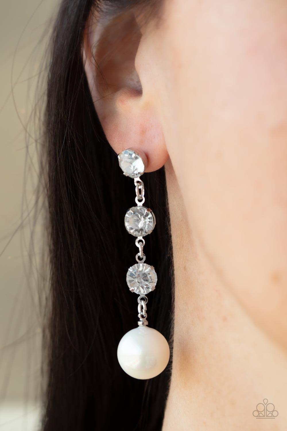 Paparazzi Accessories Yacht Scene - White Encased in sleek silver fittings, a trio of classic white rhinestones give way to an oversized iridescent pearl, creating an elegantly extended chandelier. Earring attaches to a standard post fitting. Sold as one