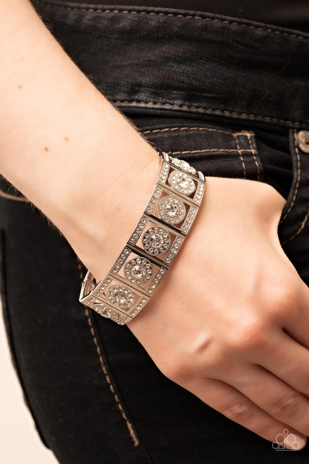 Paparazzi Accessories Ultra Upscale - White A glassy white rhinestone is pressed into a ring of glitzy white rhinestones inside a rectangular silver frame dusted in dazzling white rhinestones. The timeless frames sparkle along stretchy bands around the wr