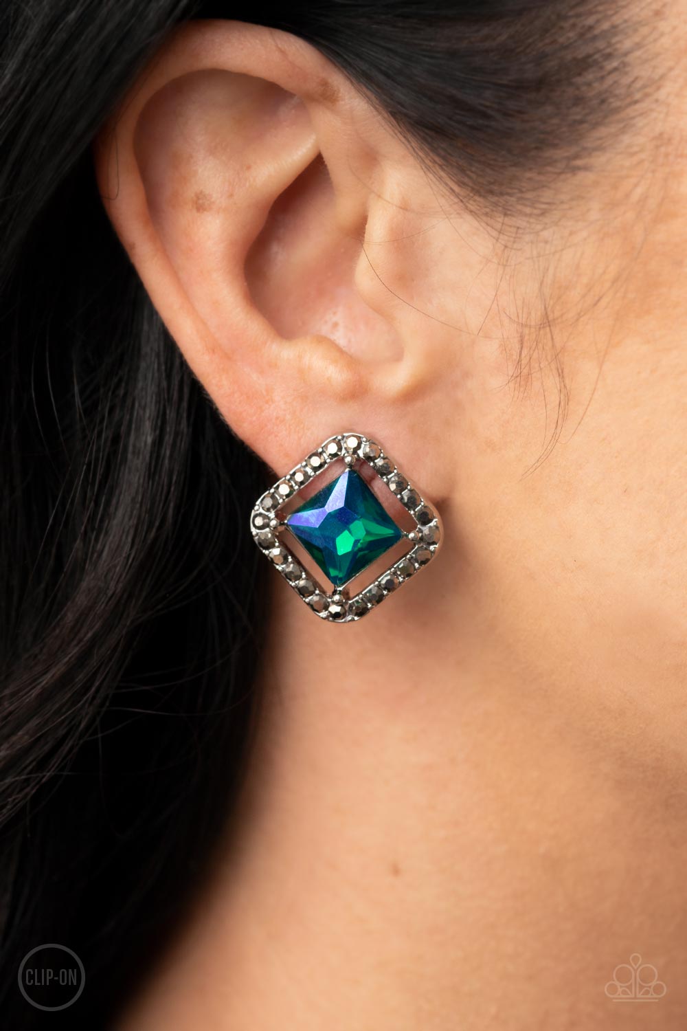 Paparazzi Accessories Cosmic Catwalk - Green *Clip-On Featuring an iridescent UV finish, an emerald cut green gem seemingly floats in the center of a hematite rhinestone encrusted frame for a stellar statement. Earring attaches to a standard clip-on fitti