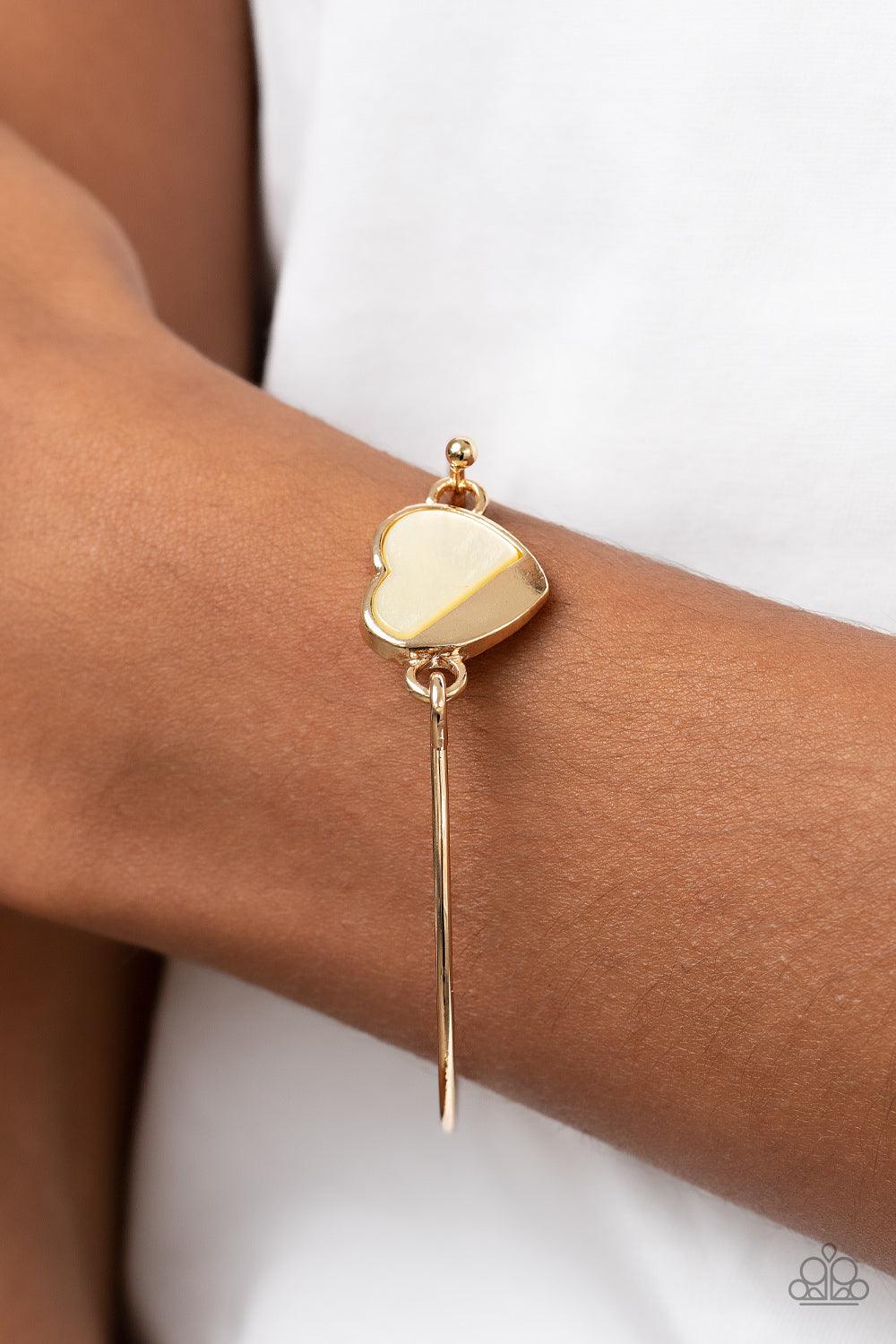 Paparazzi Accessories Hidden Intentions - Gold A glistening gold plate slants across a white shell-like heart charm that delicately hinges to a dainty gold bangle-like bracelet, creating a charming centerpiece around the wrist. Features a barbell closure.