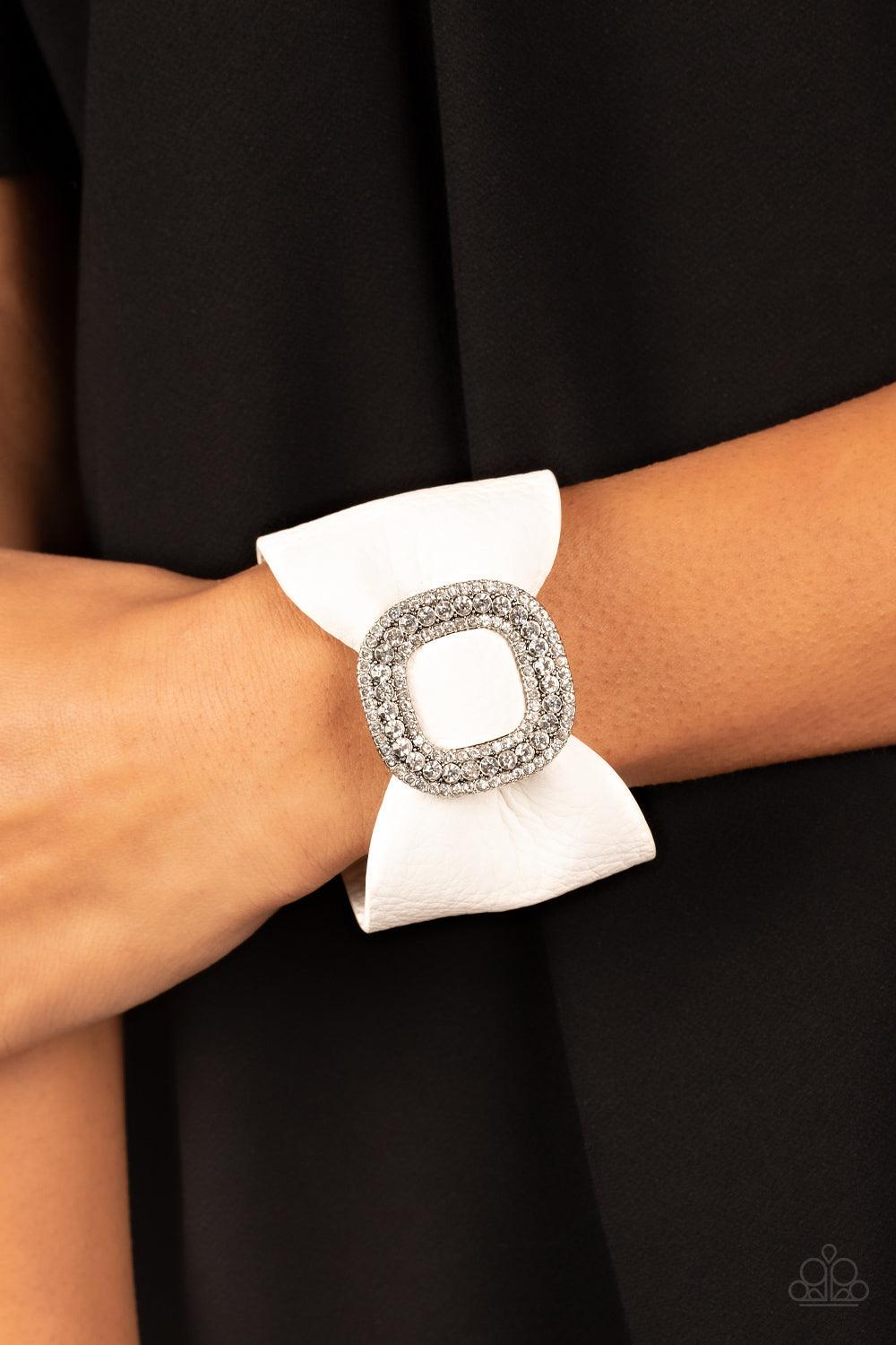 Paparazzi Accessories Lights, SELFIE, Action! - White A thick white pleather band delicately knots around the wrist. Stacked with brilliant white rhinestones, a dramatic silver buckle sparkles at the center of the wrist for a dramatic finish. Features an