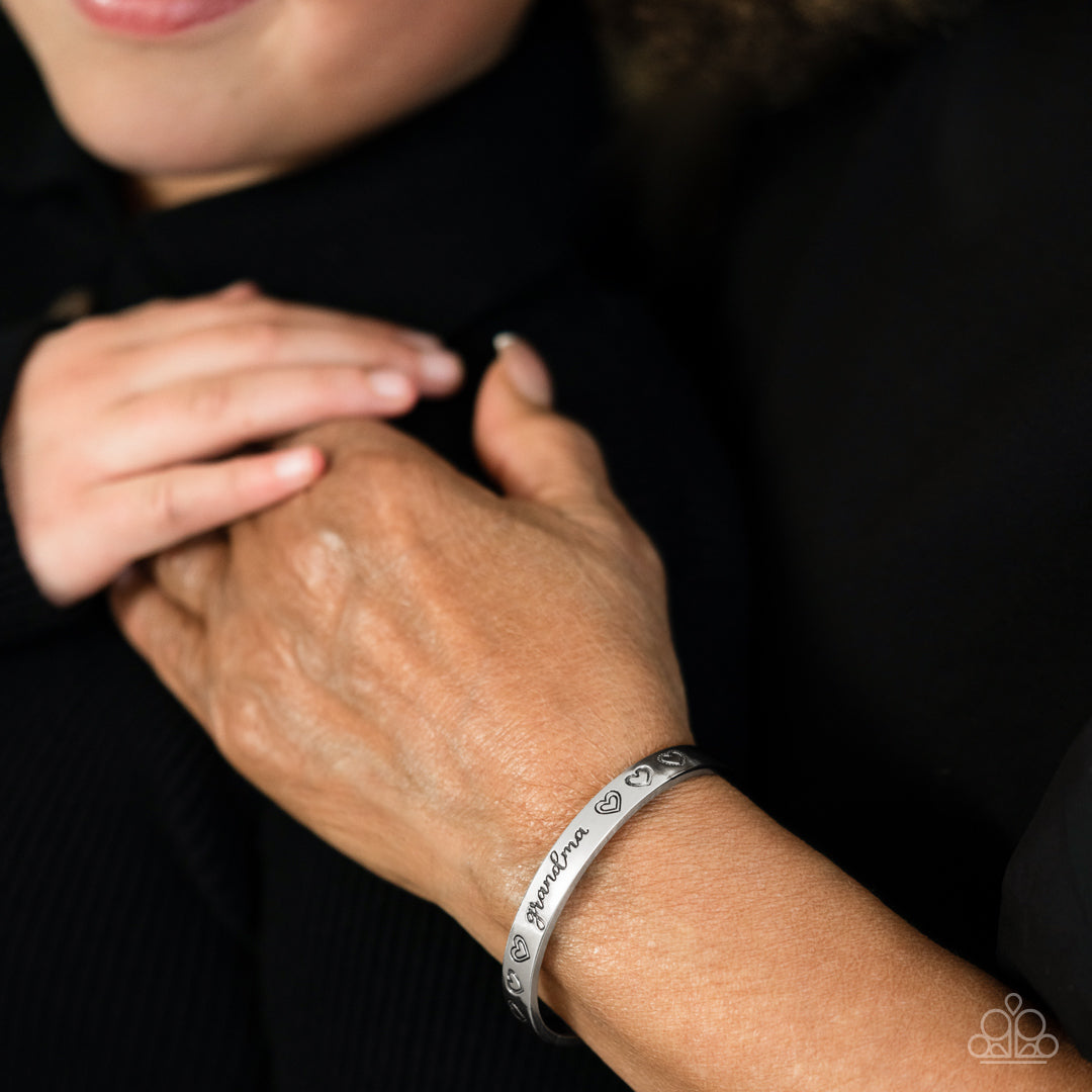 Paparazzi Accessories A Grandmothers Love - Silver Brushed in a polished sheen, a skinny silver bar curls around the wrist, creating a rustic cuff. Featuring a heart motif, the skinny cuff is engraved with the word “grandma” with various styles of hearts
