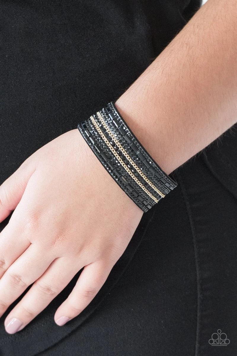 Paparazzi Accessories Rebel Radiance - Black Featuring classic round and edgy emerald style cuts, glittery black rhinestones and glistening gold chains are encrusted along bands of black suede for a sassy look. Features an adjustable snap closure. Jewelry